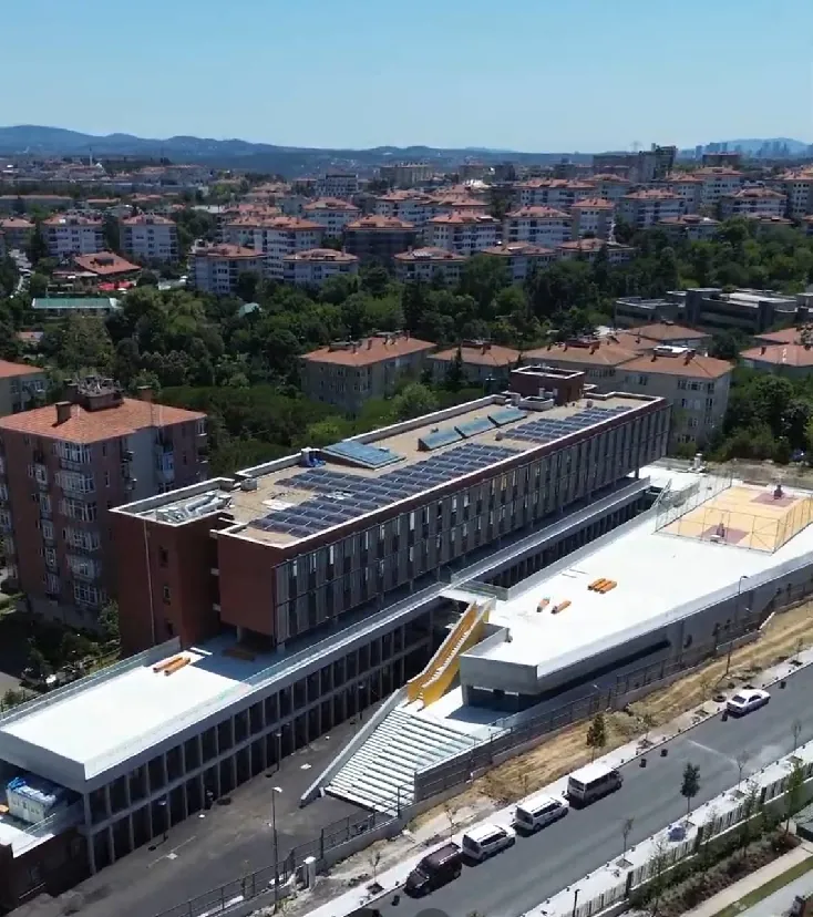 Okul binasının havadan görünümü: güneş panelli çatı, tuğla cephe ve çatıdaki spor sahası